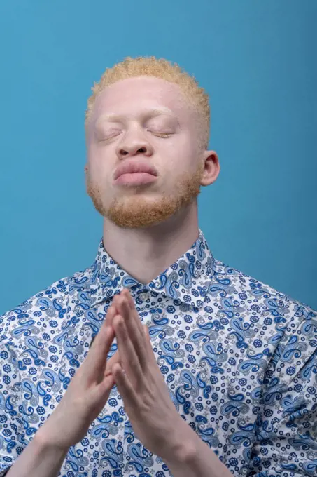 Studio portrait of albino man in blue patterned shirt with eyes closed