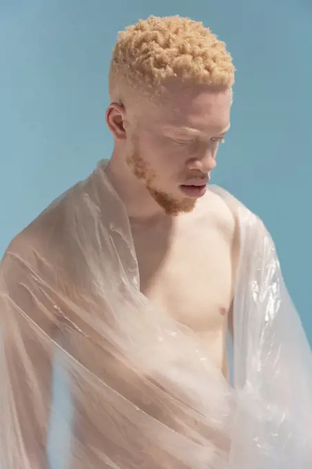 Studio portrait of shirtless albino man wrapped in plastic sheet