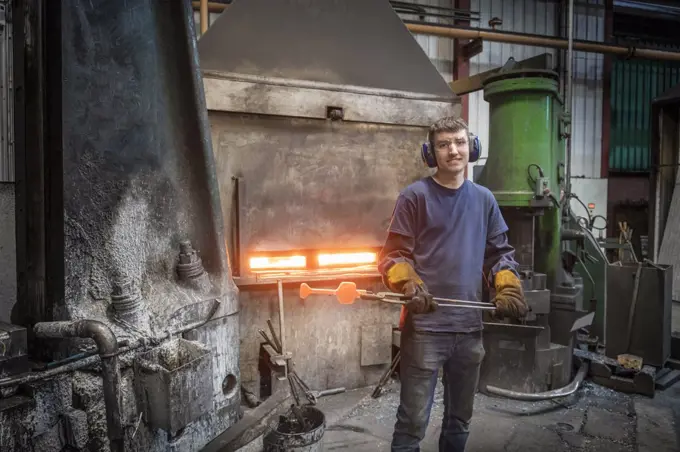 Portrait of apprentice engineer with hot titanium part in industrial forge