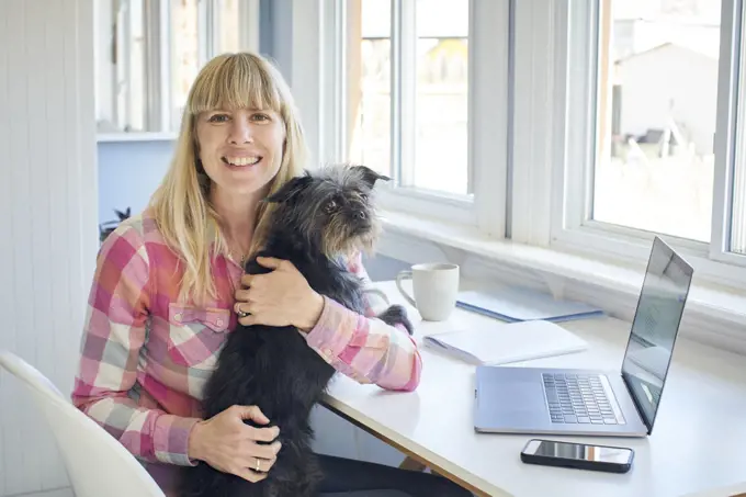 Portrait of mature woman holding dog and working from home