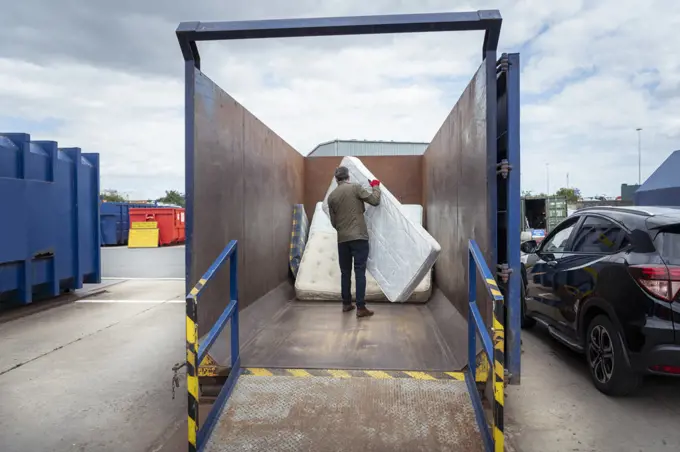 UK, Grimsby, Rear view of man unloading old mattresses at recycling center