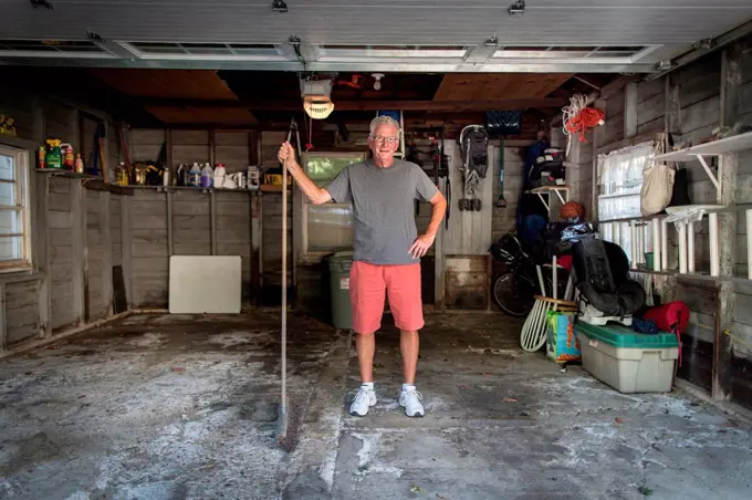 Portrait of senior man standing in garage holding broom