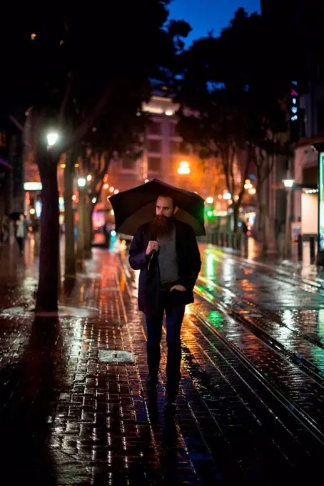 Mid adult man walking in city at night, using umbrella, Downtown, San Francisco, California, USA