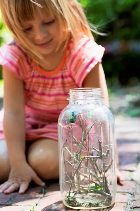 Girl kneeling to watch caterpillar jar in garden