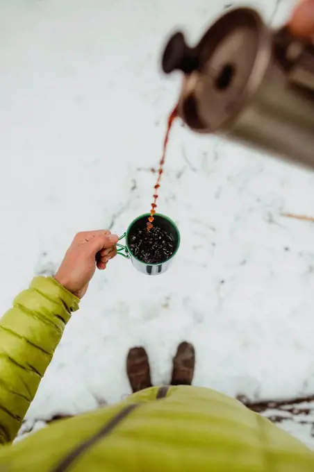 Personal perspective view of male hiker pouring coffee from flask in snow