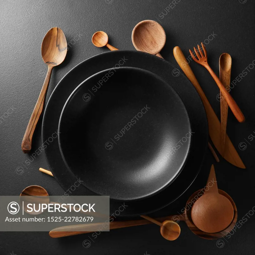 black plates and wooden spoon, fork, knife on a black table.. plates and wooden cutlery
