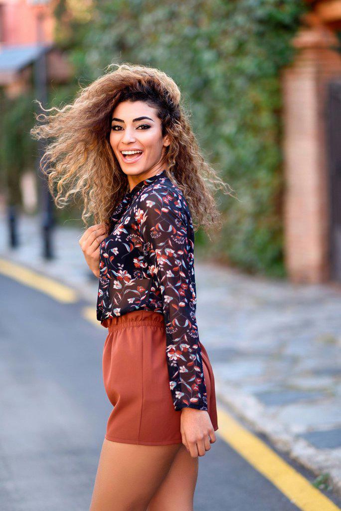 Happy young arabic woman with black curly hairstyle. Arab girl smiling in the street moving her hair.