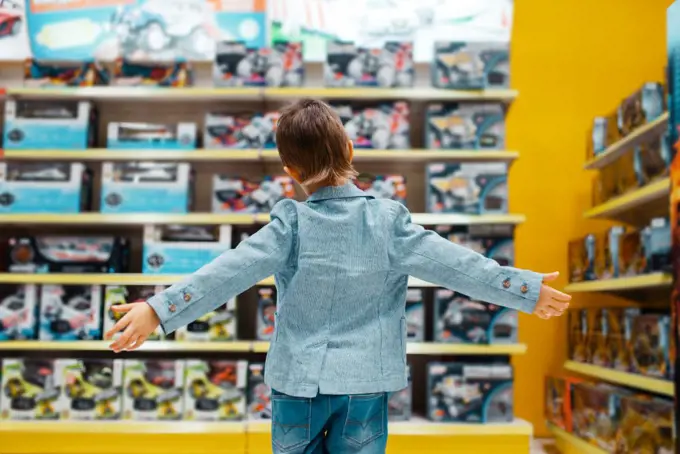Little boy at the shelf in kids store, back view. Son choosing toys in supermarket, family shopping. Little boy at the shelf in kids store, back view