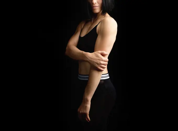 Adult girl with a sports figure in black bra and black shorts standing on a dark background, muscular body, black hair