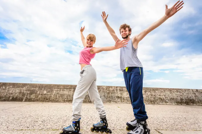 Outdoors activities sport and hobby. Exercises for healthy and strong body. Friends stretch together have fun riding rollerblades stand with outstretched arms.. Two people on rollerblades with spread arms.