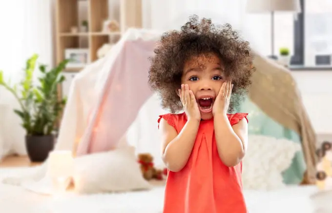 childhood, expressions and emotions concept - surprised or scared little african american girl screaming over kids tent or teepee at home background. surprised or scared little african american girl