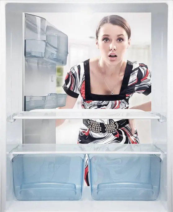 Young woman looking on empty shelf in fridge.