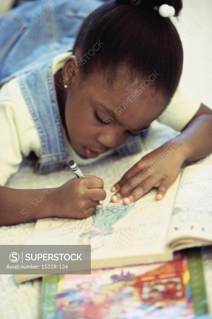 Stock Photo: 1531R-134 Girl lying on the floor coloring with crayons in a book