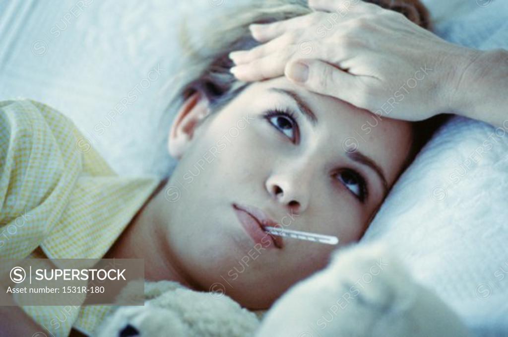 Stock Photo: 1531R-180 Young woman lying in bed with a thermometer in her mouth and a hand on her forehead