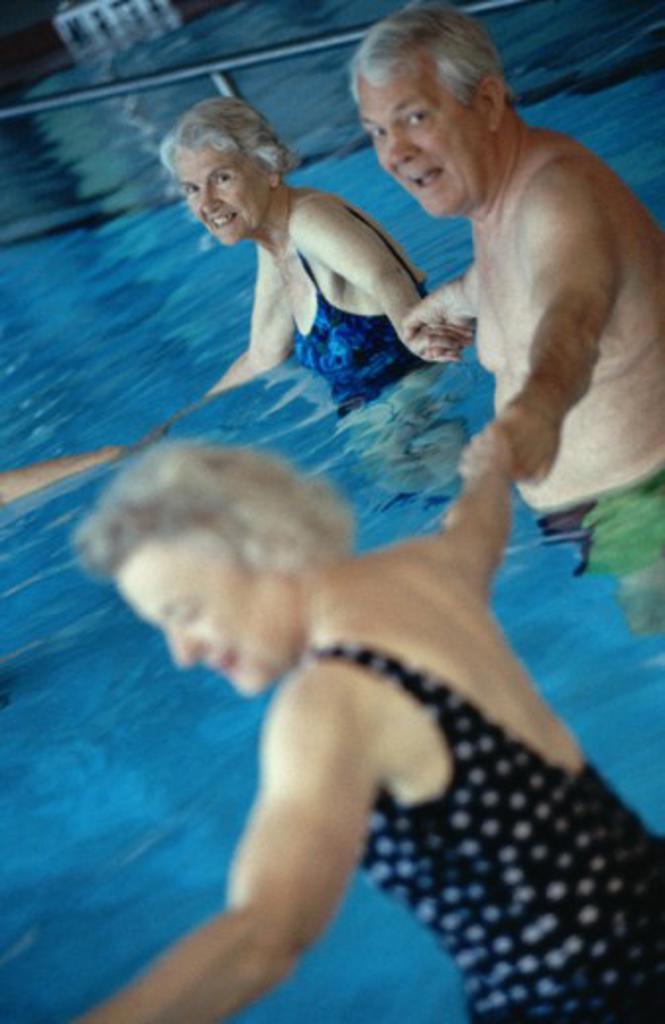 Portrait of a senior man holding hands with two senior women in a swimming pool