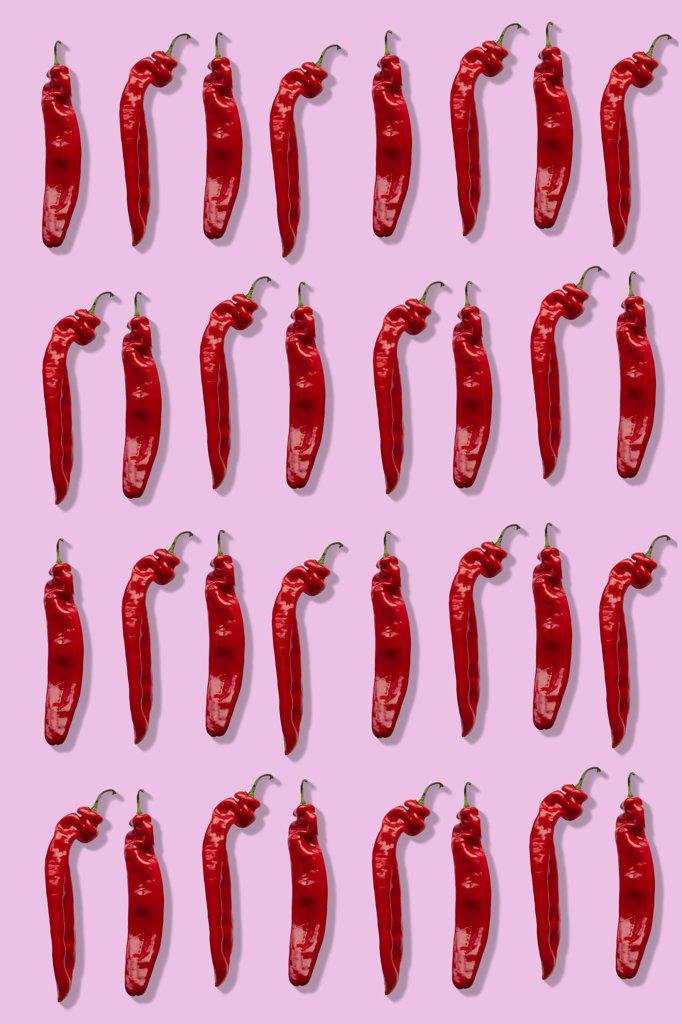 Four rows of red chillies on a pink background