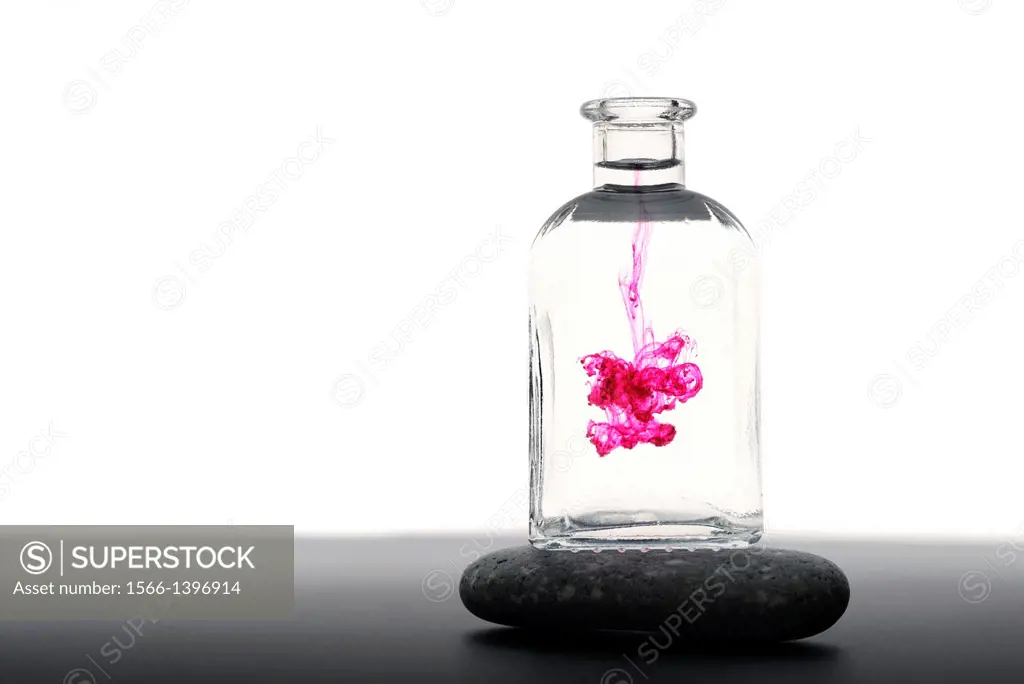 A drop of magenta liquid dissolving in a glass bottle with water.