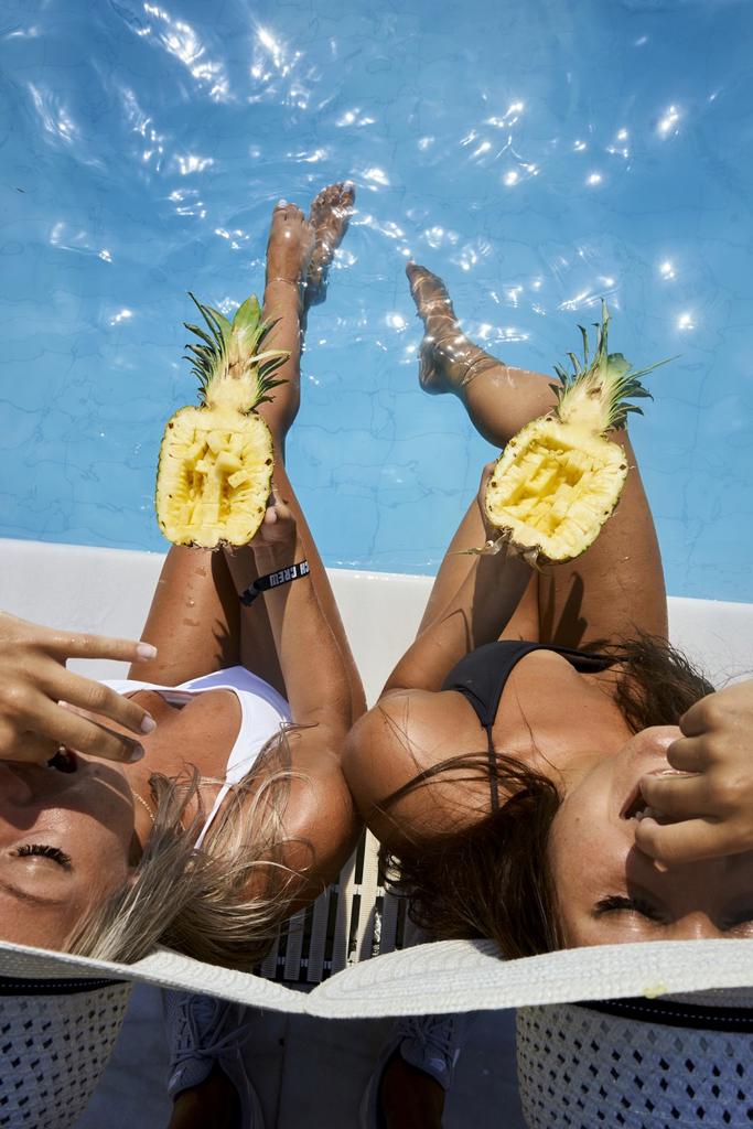 Two young women by the pool, eating pineapple. Chersonissos, Crete, Greece.