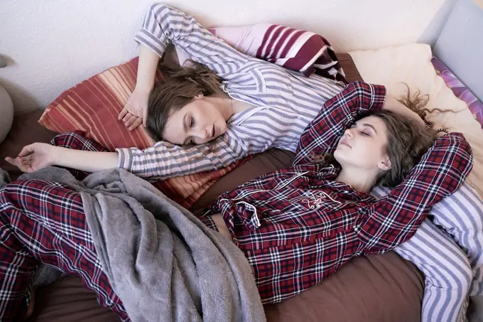 two young women laying in bed together, wearing pyjamas