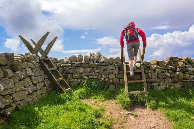 A hiker crosses a stile on the Hadrians Wall Walk at Crag Lough in Northumberland, England, UK.
