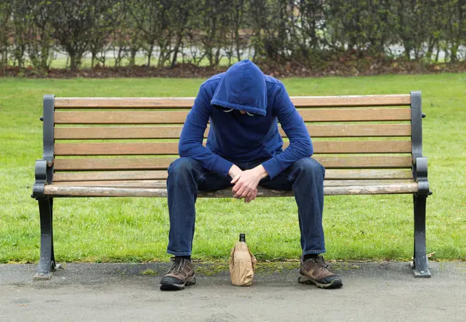 Male wearing hoodie drinking in public park in England. United Kingdom.