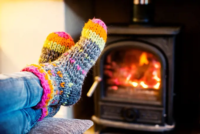 Feet warming up with a hand made colored socks in a position of rest and relax near a wood stove in winter.