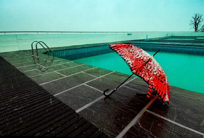Red umbrella covered with snow at poolside, after season symbol, Geneva, Switzerland, snow fall