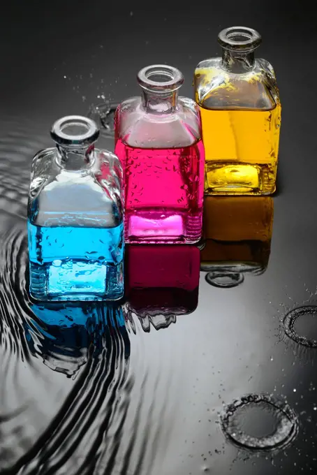 Cyan, magenta, yellow liquids in bottles on water and black background, and a close up of water droplets splashing.
