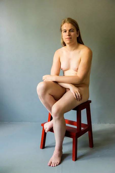 Tilburg, Netherlands. Studio portrait of a young, nude transgender sitting on a stool.