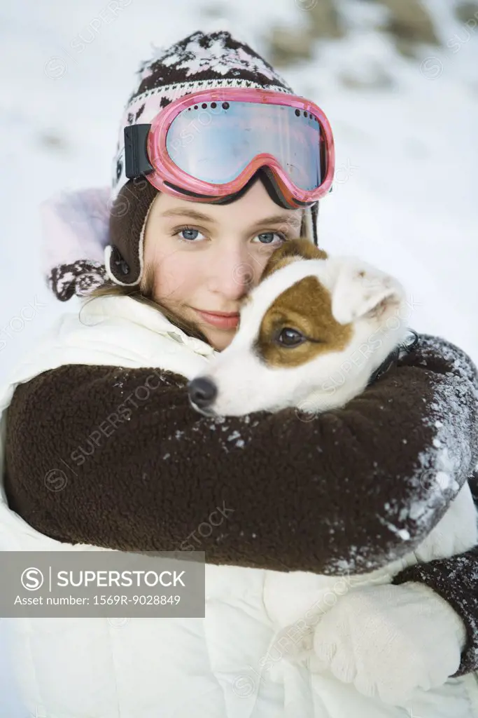 Teenage girl embracing dog, dressed in winter clothing, smiling at camera, portrait