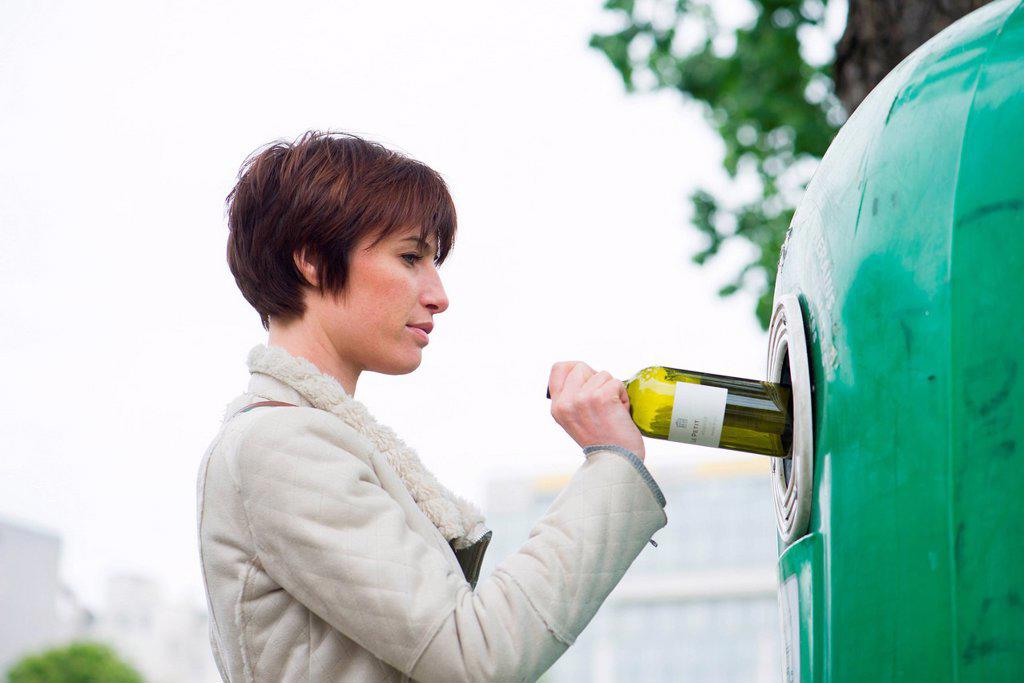 Woman putting wine bottle into recycling bin