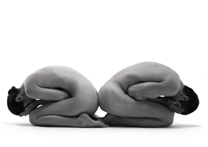 Nude man and woman curled up with hands on face, back to back, b&w