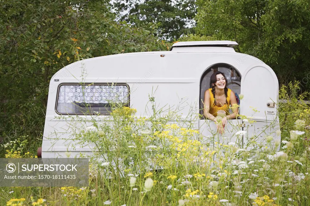 Happy young woman in camper trail in meadow