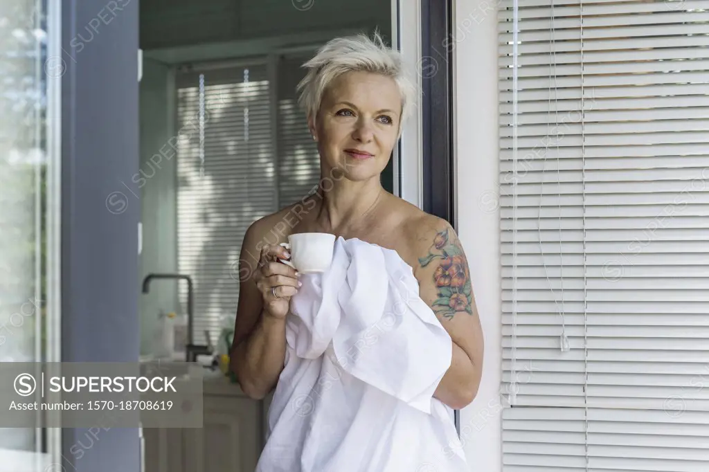 Woman with tattoo wrapped in sheet drinking coffee