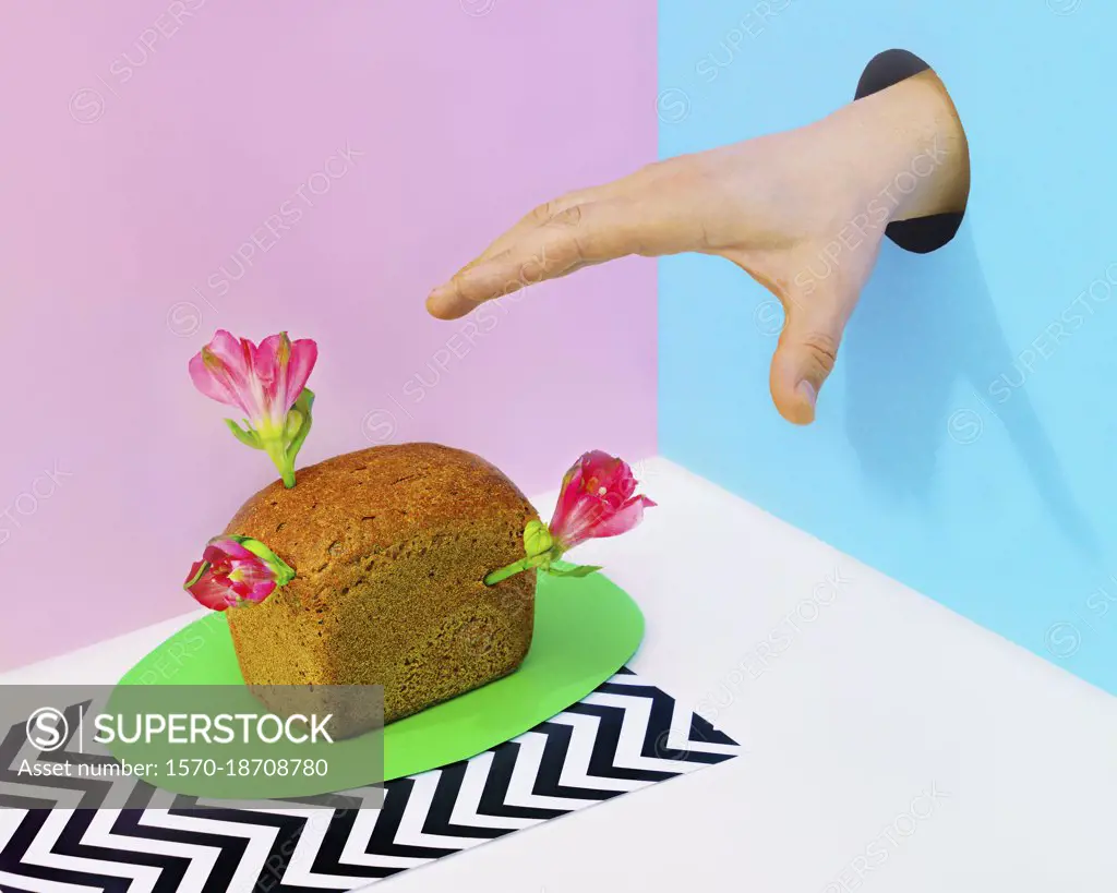 Hand in hole reaching for mini loaf of bread with flowers