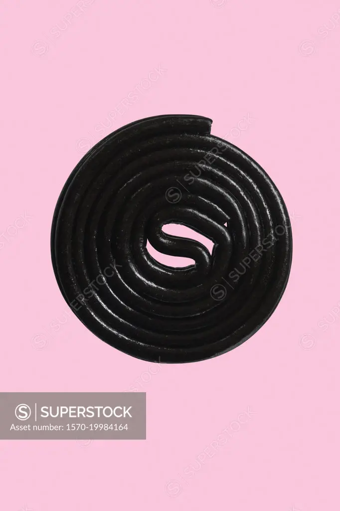 Close up black licorice coil on pink background