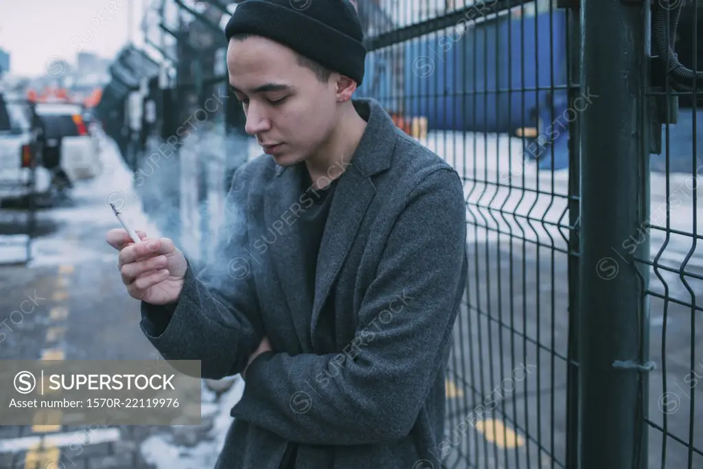 Young man smoking along winter fence