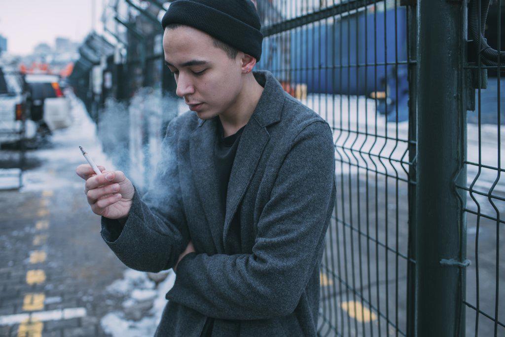 Young man smoking along winter fence