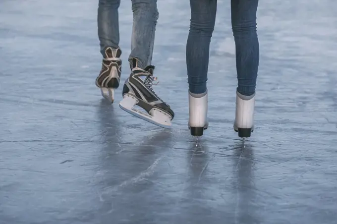 Low section of couple ice-skating on rink