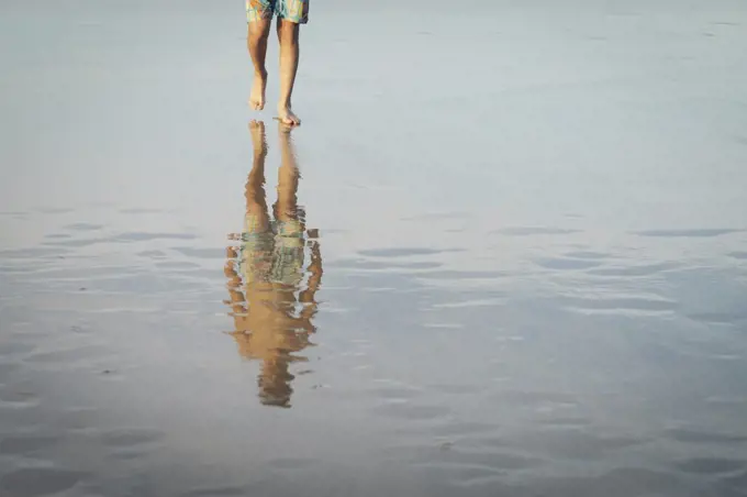 Teenage boy walking on wet sand beach
