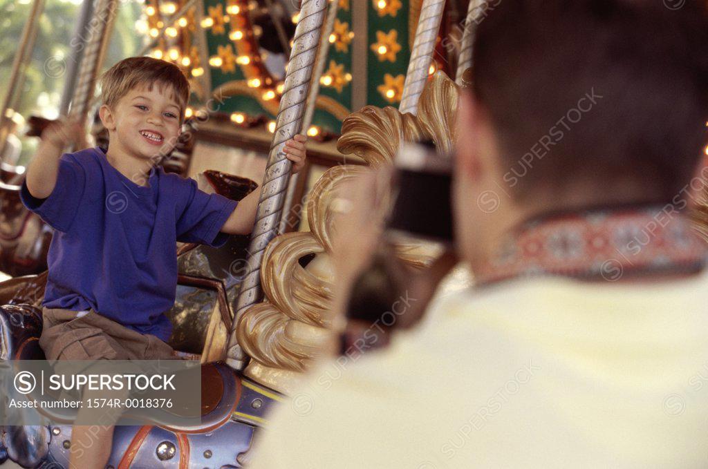 Stock Photo: 1574R-0018376 Rear view of a father taking a photograph of his son riding a carousel horse
