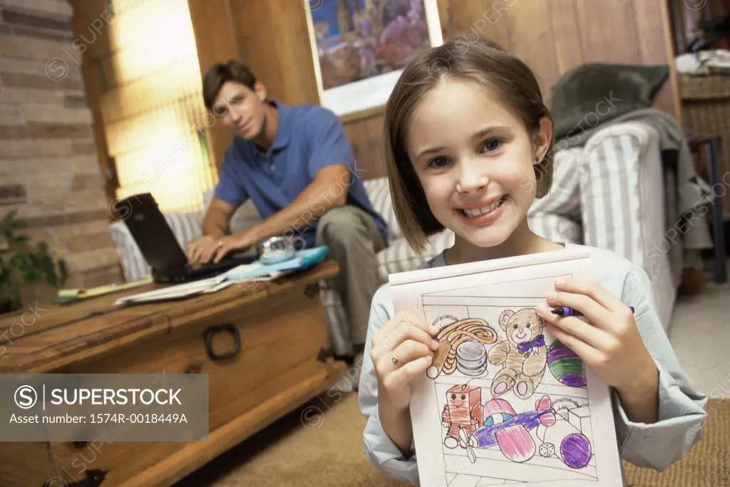 Portrait of a girl showing her drawing with her father sitting behind her