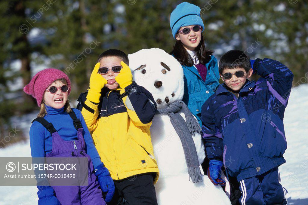 Stock Photo: 1574R-0018498 Portrait of two boys and two girls standing beside a snowman