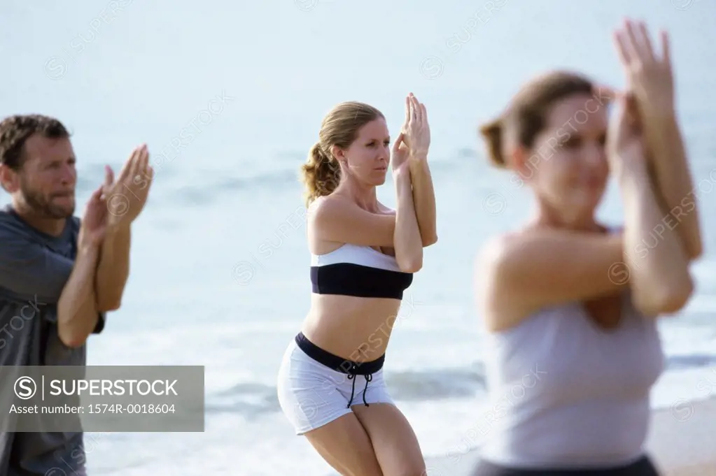 Two young women and a mature man exercising on the beach