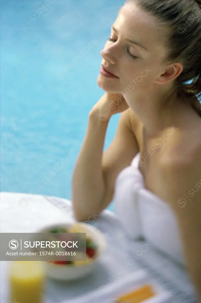 High angle view of a young woman sitting with her eyes closed at poolside