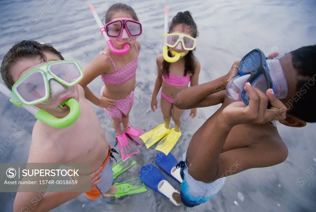 High angle view of two boys and two girls wearing snorkel masks and flippers on the beach