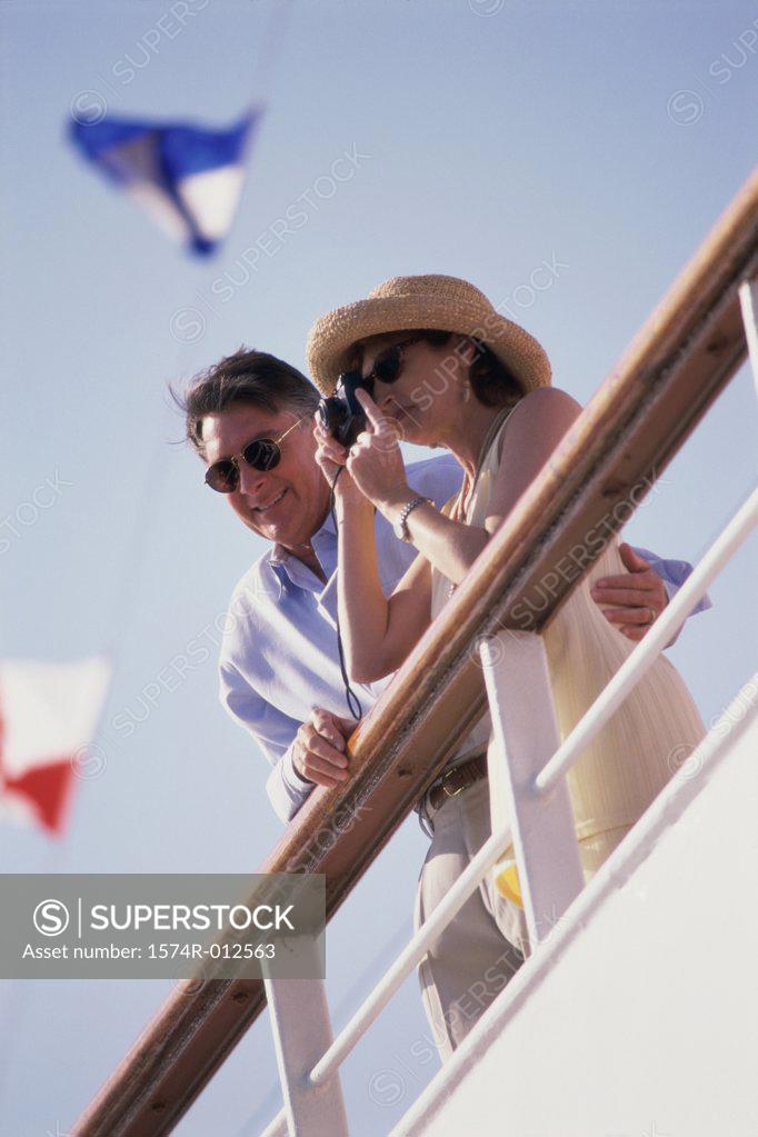Stock Photo: 1574R-012563 Low angle view of a mature woman taking a photograph with a mature man standing beside her on a cruise ship