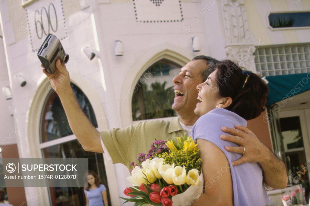 Stock Photo: 1574R-012807B Side profile of a mature couple taking a photograph of themselves in a market