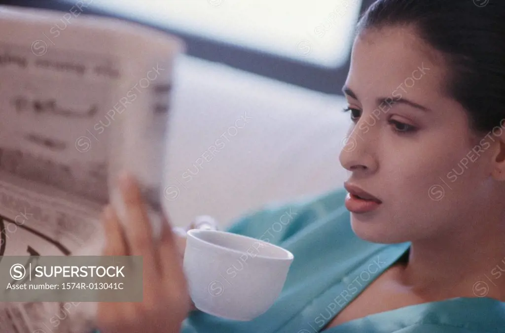 Close-up of a young woman reading a newspaper and drinking coffee
