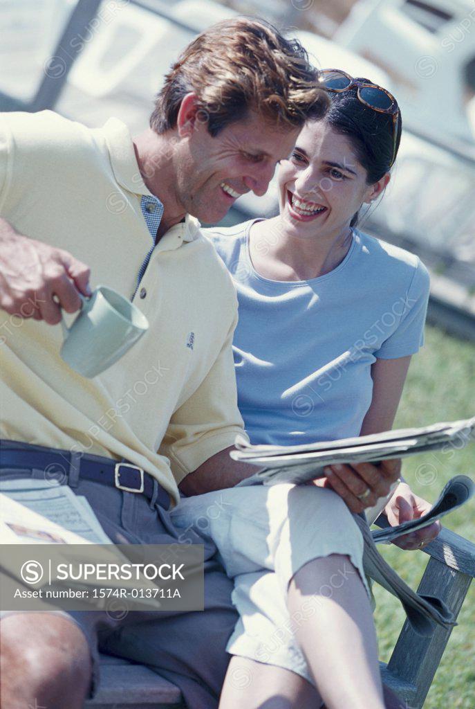 Stock Photo: 1574R-013711A Mid adult man reading a newspaper with a woman sitting beside him